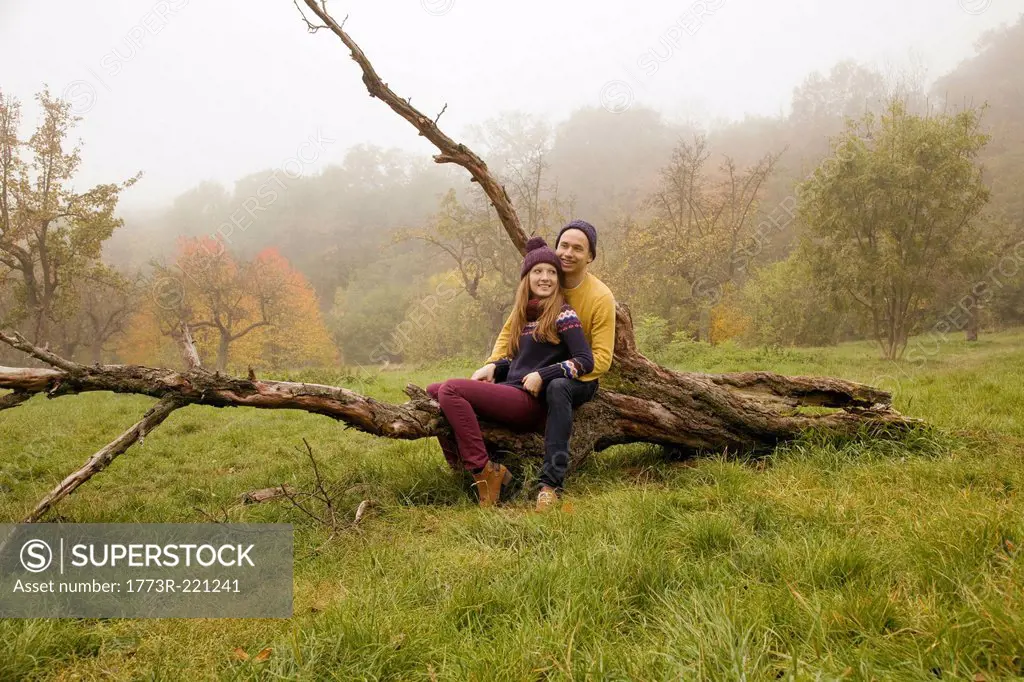 Young couple sitting on bare tree in misty park