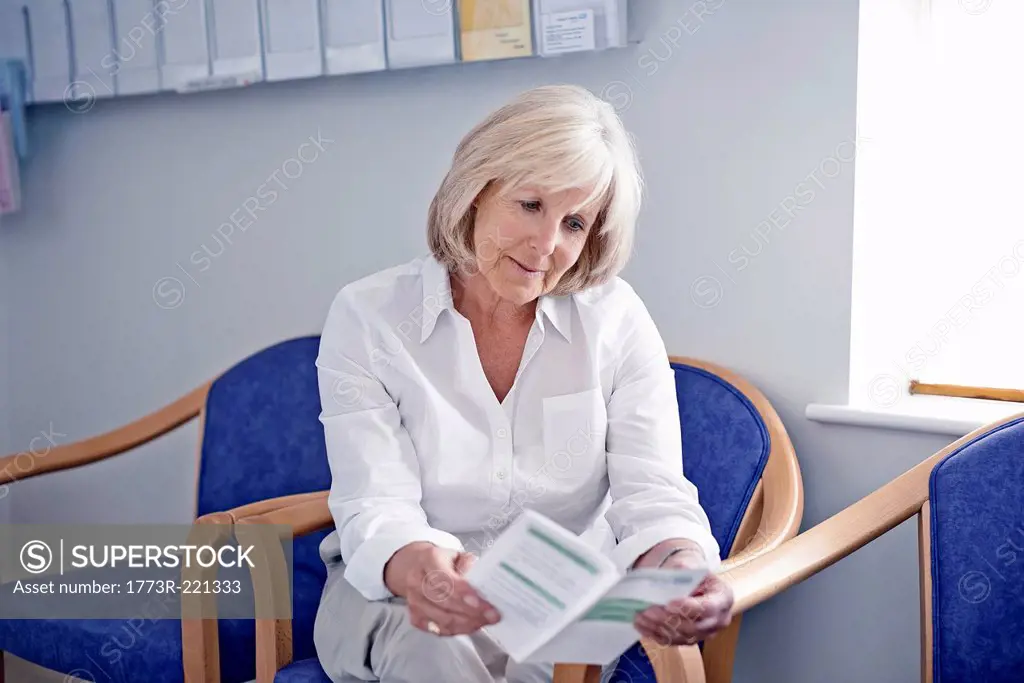 Mature female patient reading leaflet in hospital waiting room