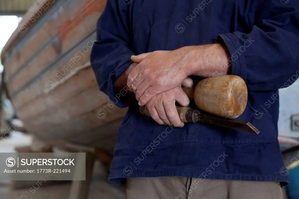 Close up of carpenters hands holding chisel in boat workshop