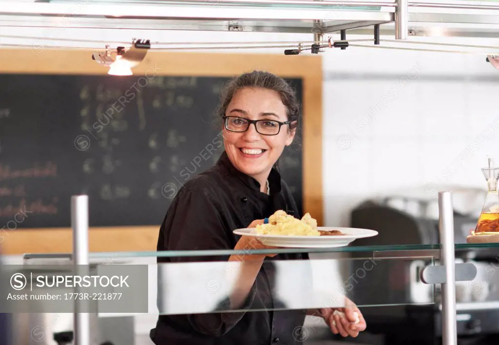 Woman working in restaurant kitchen, serving meal