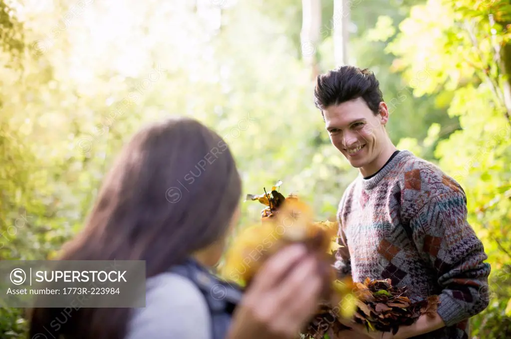 Young couple playing with autumn leaves in forest