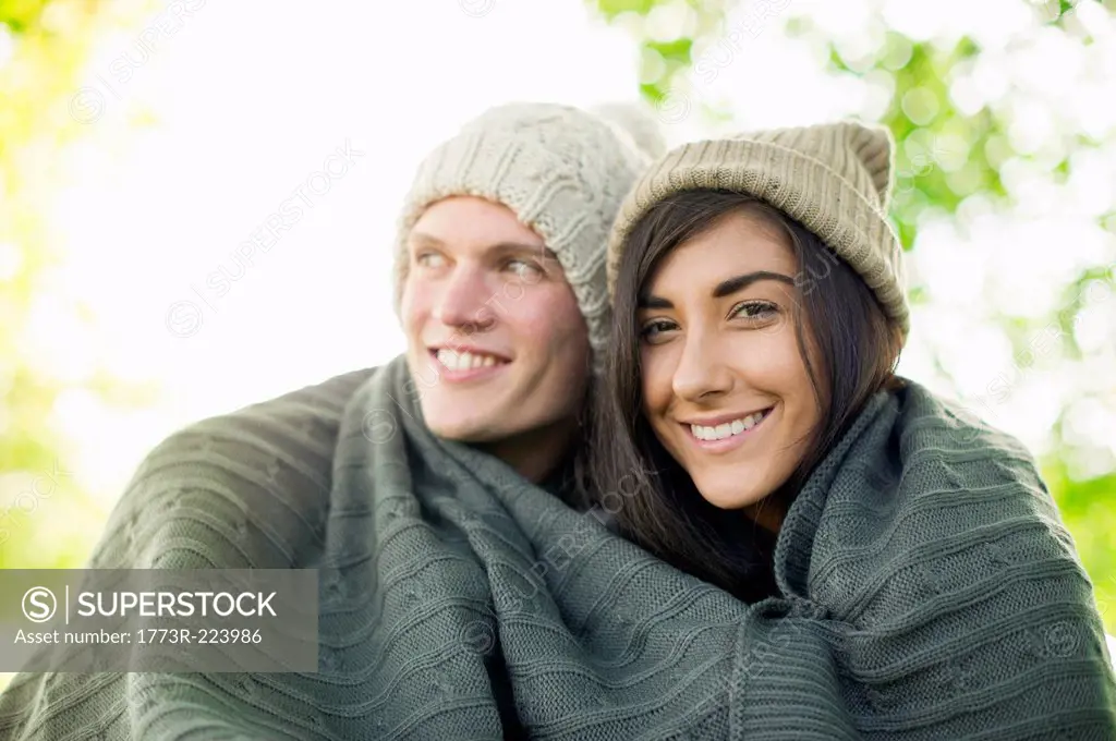 Young couple wearing knit hats wrapped in blanket