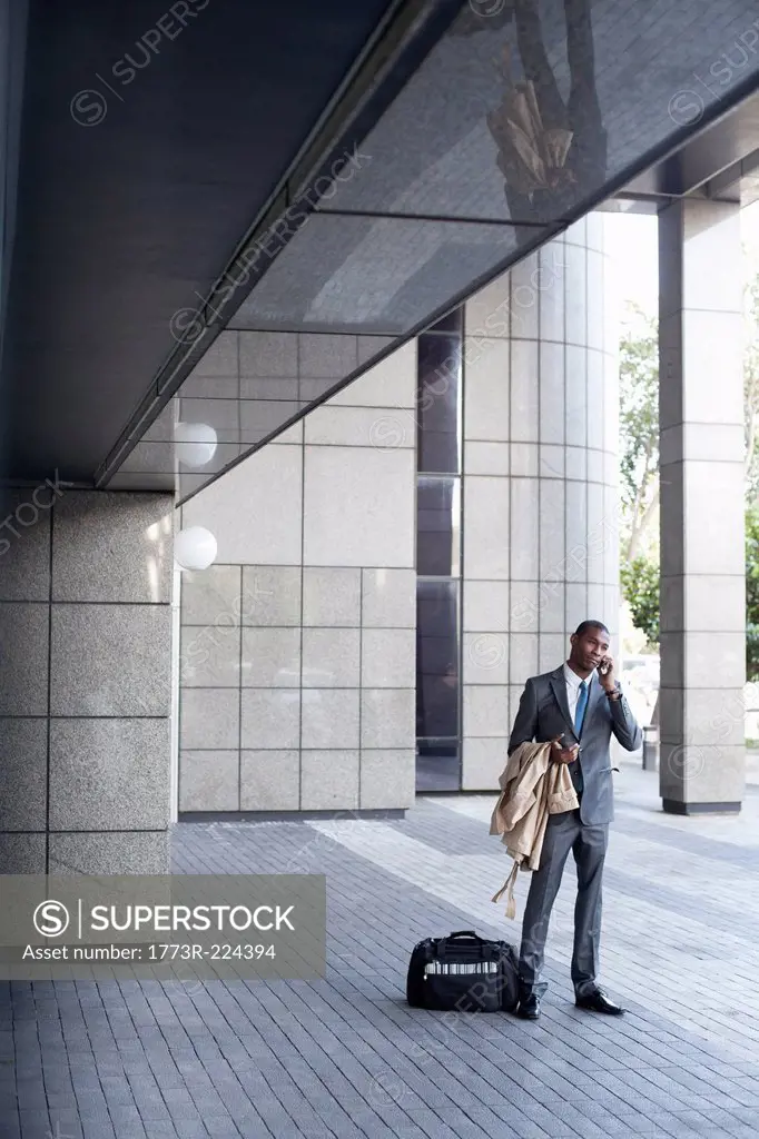 Businessman standing outside with bag and coat