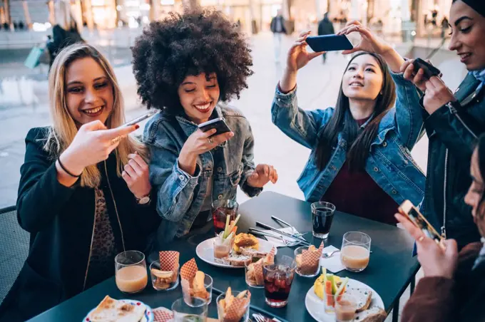 Friends taking photos of their food and drinks at outdoor cafe, Milan, Italy