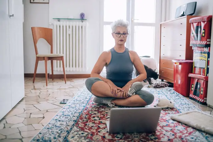 Woman sitting on floor, following online yoga class