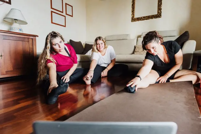Female friends stretching, taking online exercise class together