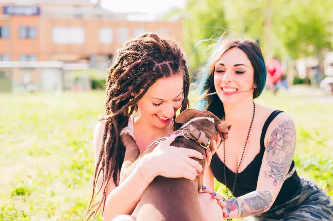 Tattooed young women playing with pit bull terrier in urban park