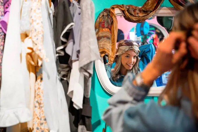 Mirror image of young woman trying on vintage clothes in thrift store