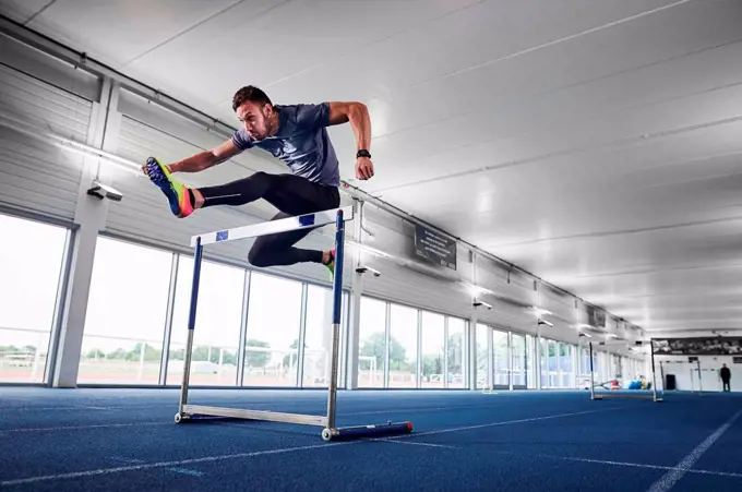 Athlete jumping over hurdle on indoor running track