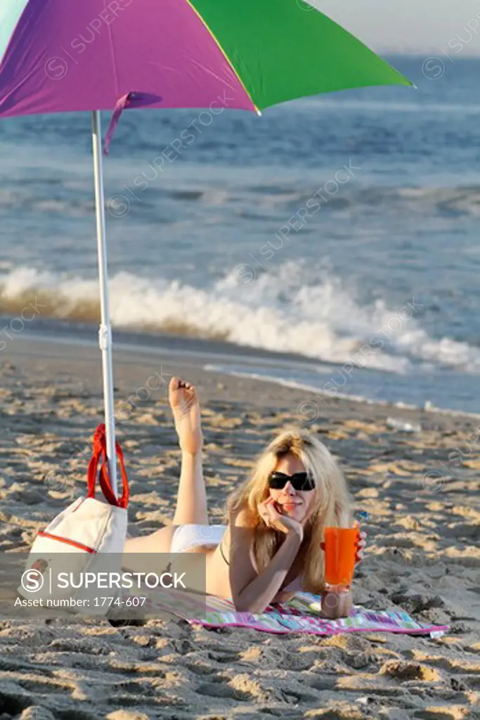 Happy young woman laying on beach with drink