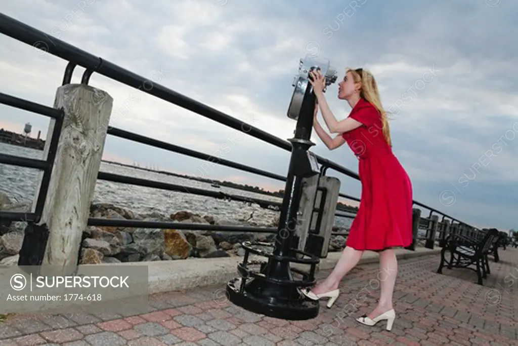 USA, New Jersey, Jersey City, Liberty State Park, Woman in red dress looking through binocular, Low angle view