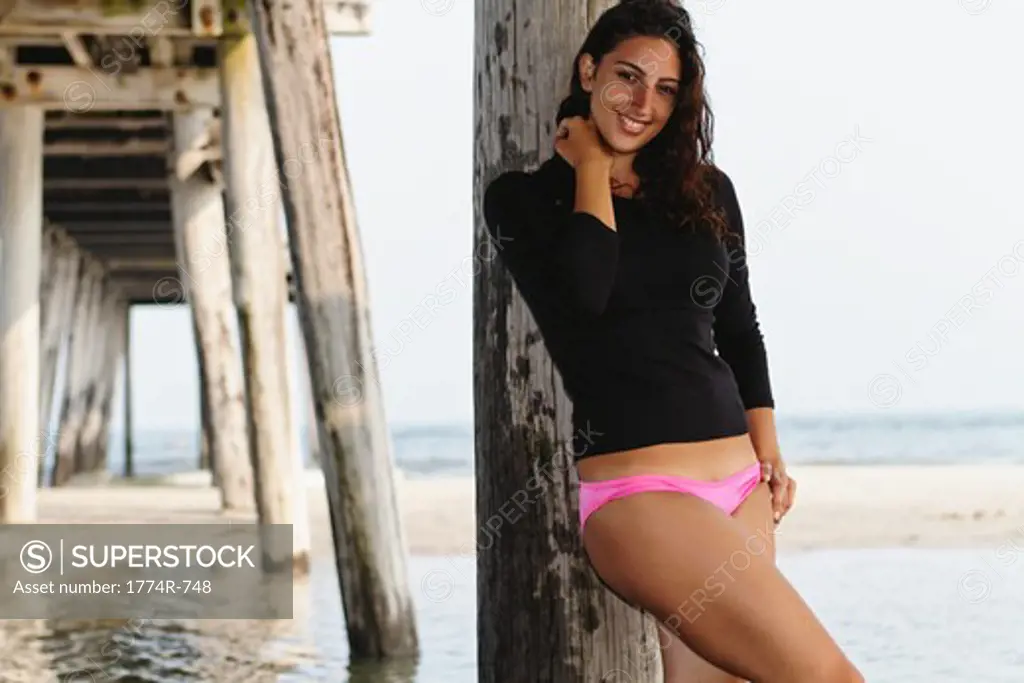 USA, New Jersey, Ocean City, Young Brunette Woman Leaning Against Pier Post on Beach and Smiling