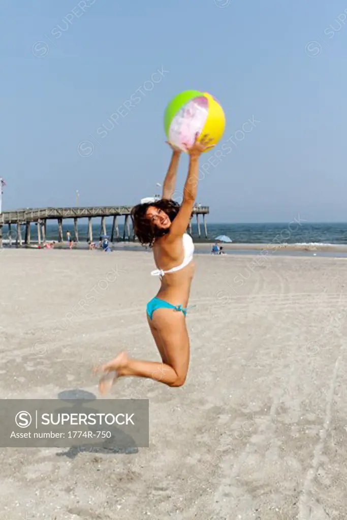 USA, New Jersey, Ocean City, Woman in Bikini Jumping Up to Catch Beach Ball on Beach
