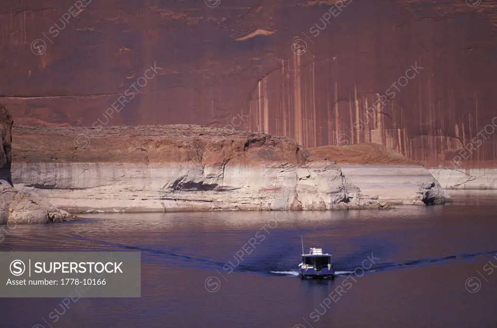 A houseboat moves away from the water's edge and a cliff