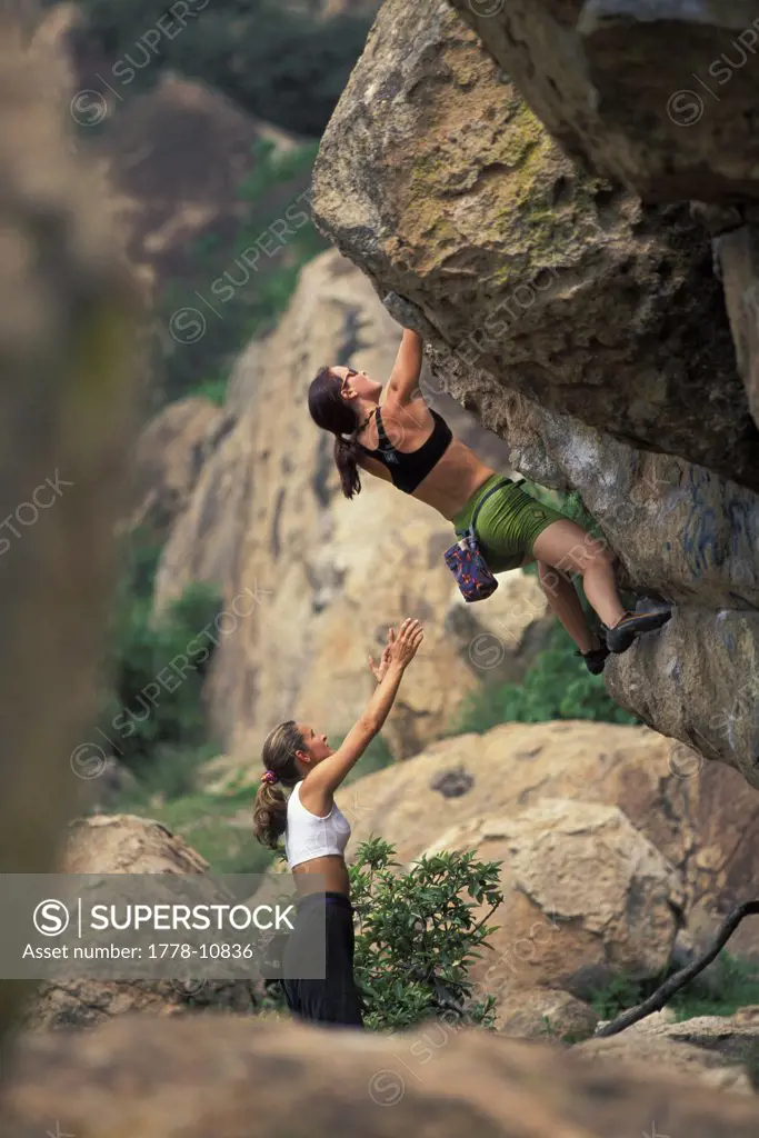 A female rock climber spots another woman as she boulders on an overhanging bouldering problem