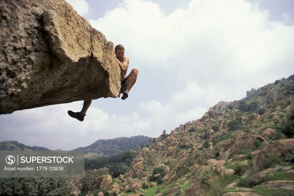 A male rock climber attempts to get over the top of an overhanging bouldering route in a remote climbing area
