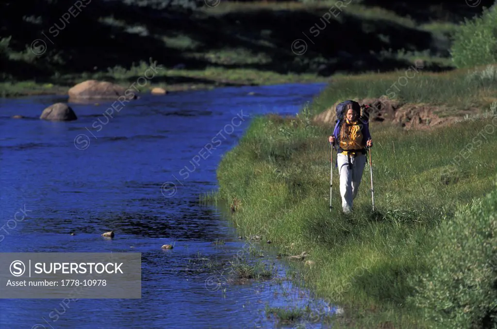 A woman trekking through a meadow next to a river