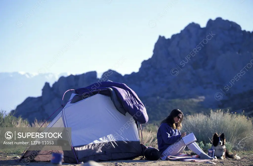 A woman writing in her journal, tent camping in the desert with her dog