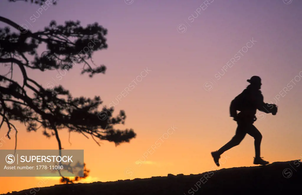 A woman trail running is silhouetted by the setting sun