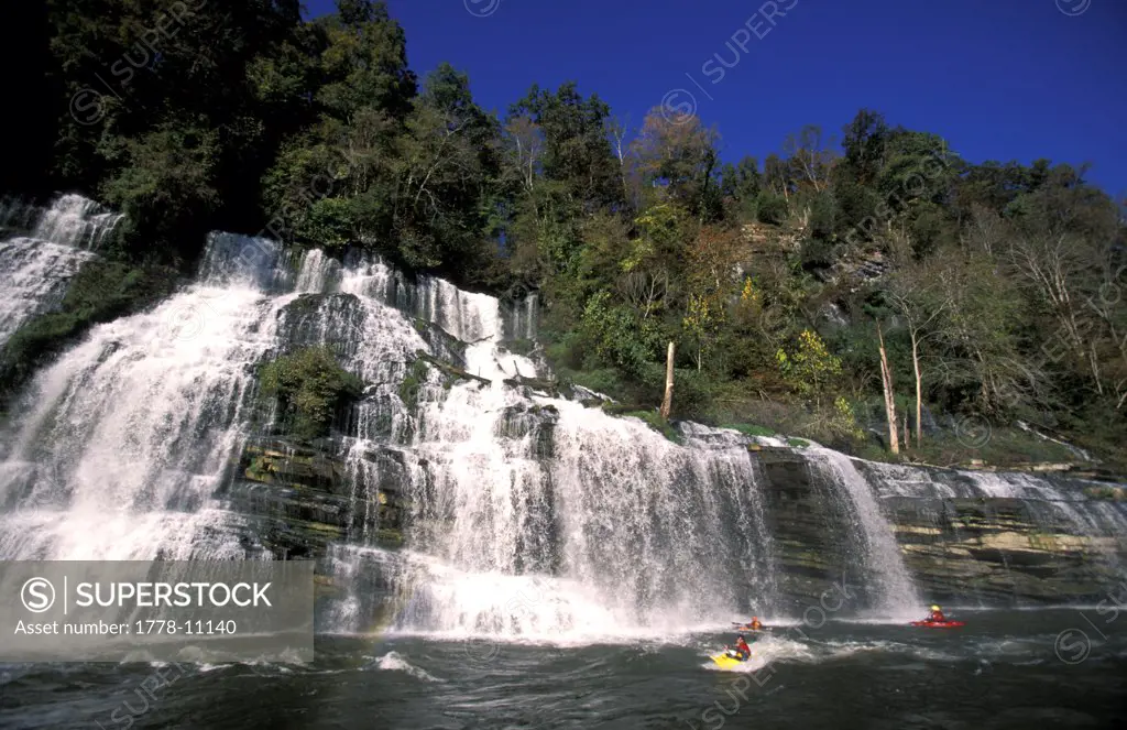 A family of kayakers surfing under a waterfall