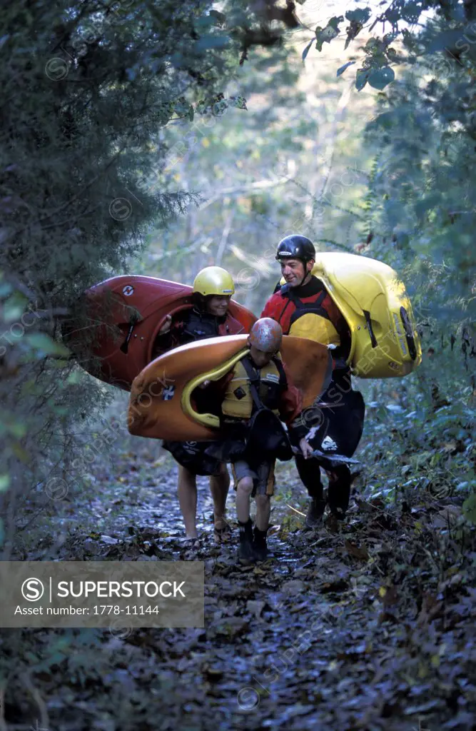 A father and his children carry their kayaks through a forest