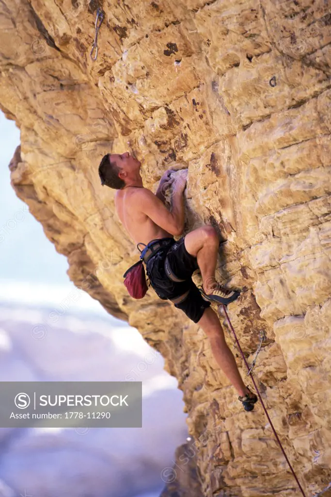 A male rock climber climbs on an overhanging climbing in the desert