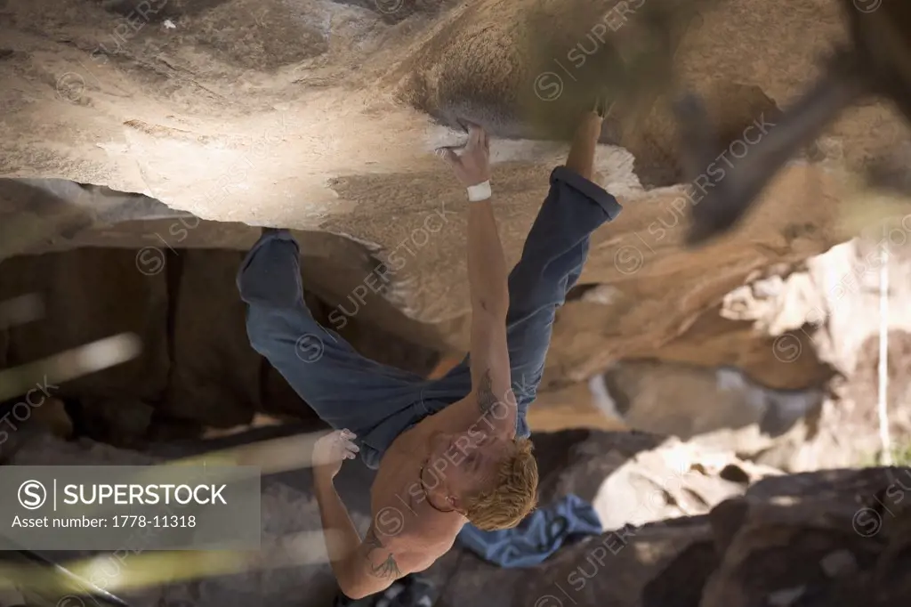 Man hangs upside down from his heels and one arm while bouldering in Hueco Tanks State Park, Texas