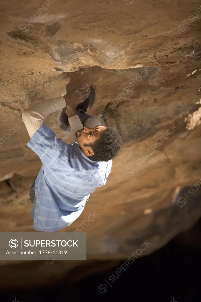 Black male reaching for a hold while boulding on a large roof at Hueco Tanks State Park, Texas