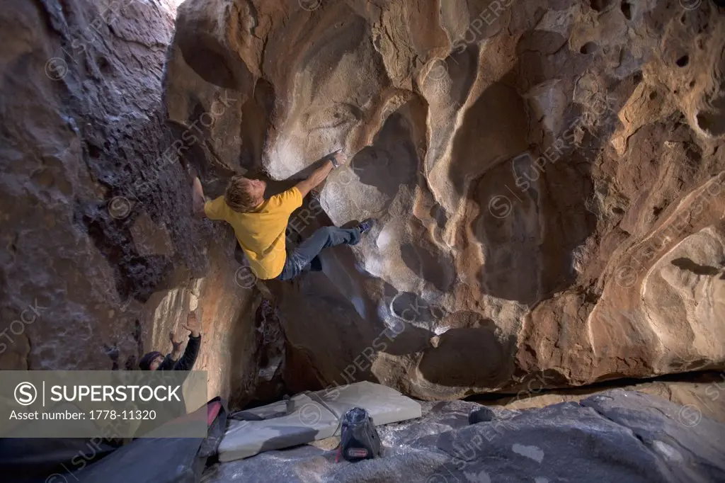 Male rock climber squeezes with all four limbs while bouldering in a dark cave in Hueco Tanks State Park Texas