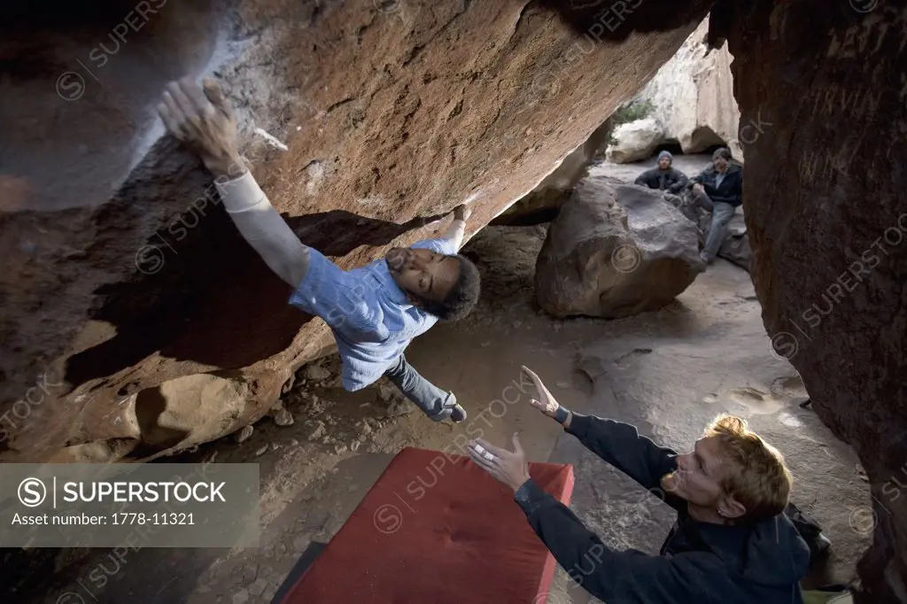 Black male makes a big reach with his left had to a large hand hold while bouldering in Hueco Tanks State Park, Texas