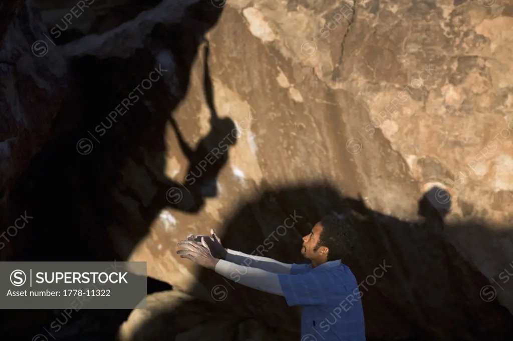 A man spots a climber, whose shadow is cast on a rock face