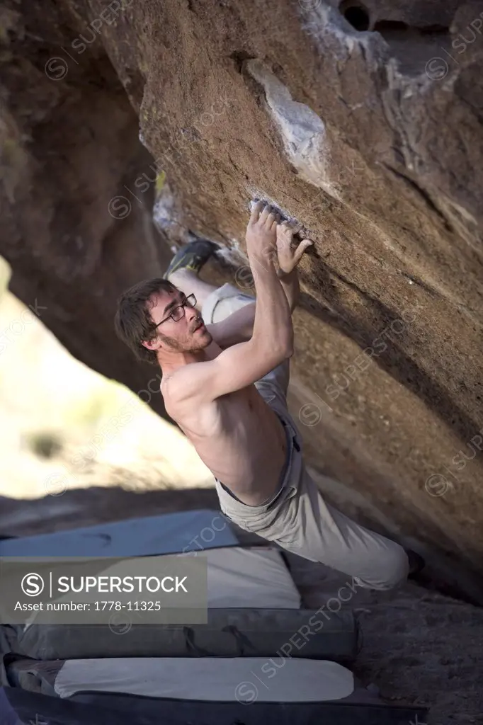 Man, with an intense expression, bouldering over a crash pad