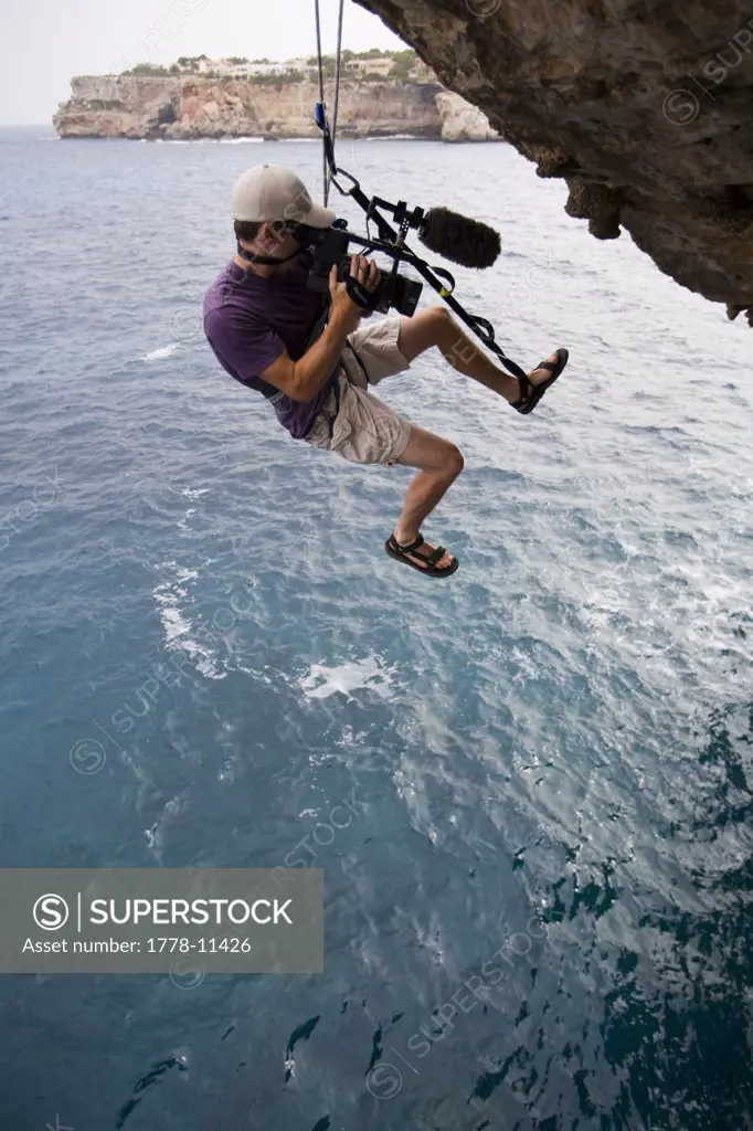 A man hanging on a rope above the ocean and filming video