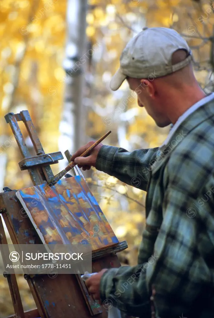 An artist paints outside in aspens on a creek, near Aspendell, California