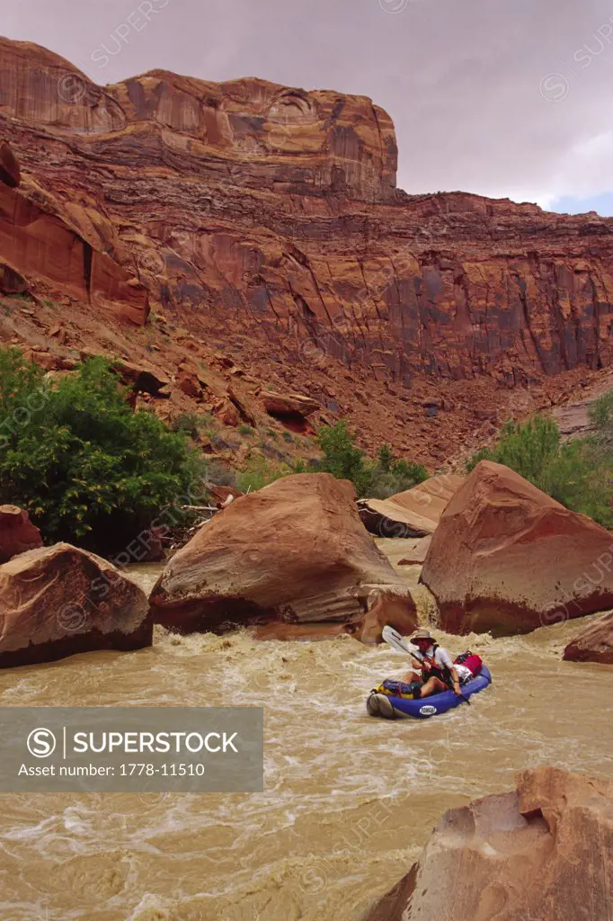man in infatable kayak going down river in desert, Escalante, Utah