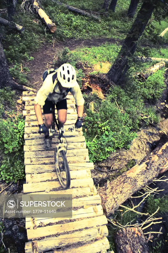 man riding mountain bike across wooden bridge, Idaho (color manipulated for effect)
