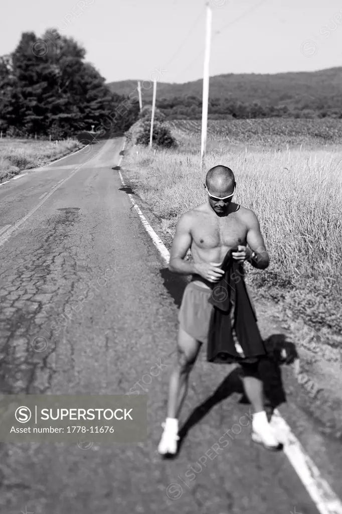 A muscular man cools down after the effort of a hot summer run on a country road in Lyme, New Hampshire