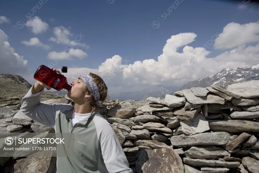 A teenage boy hiking in Vanoise National Park, High Alps, France takes a sip from his water bottle