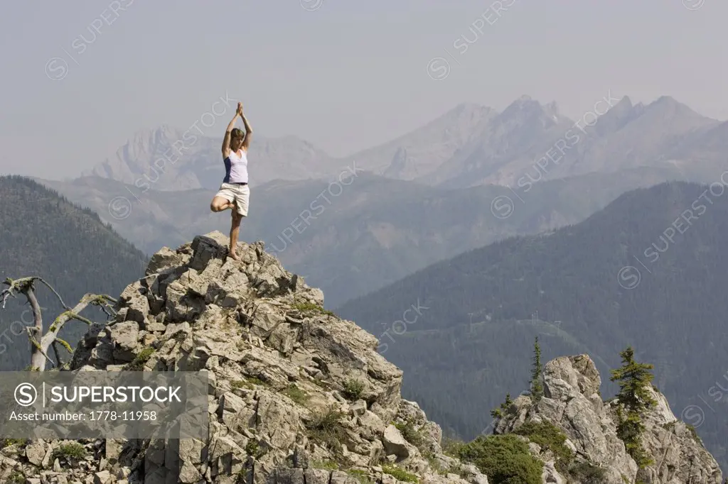 Young woman practices yoga on mountaintop at Island Lake Resort in the Lizard Range near Fernie, British Columbia, Canada