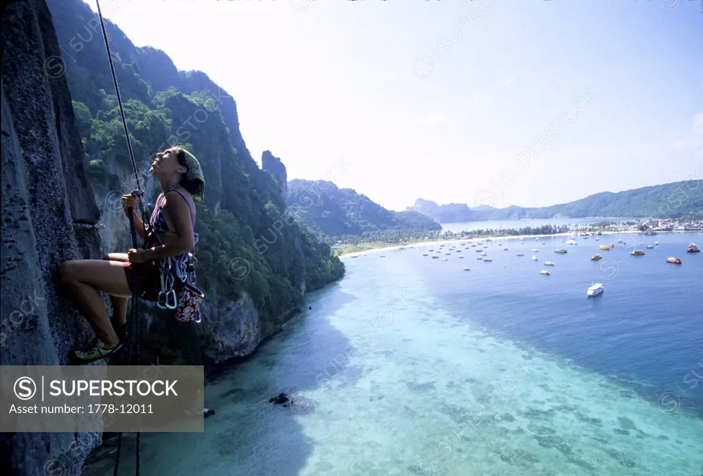 A woman rappels a limestone cliff above the ocean in Thailand