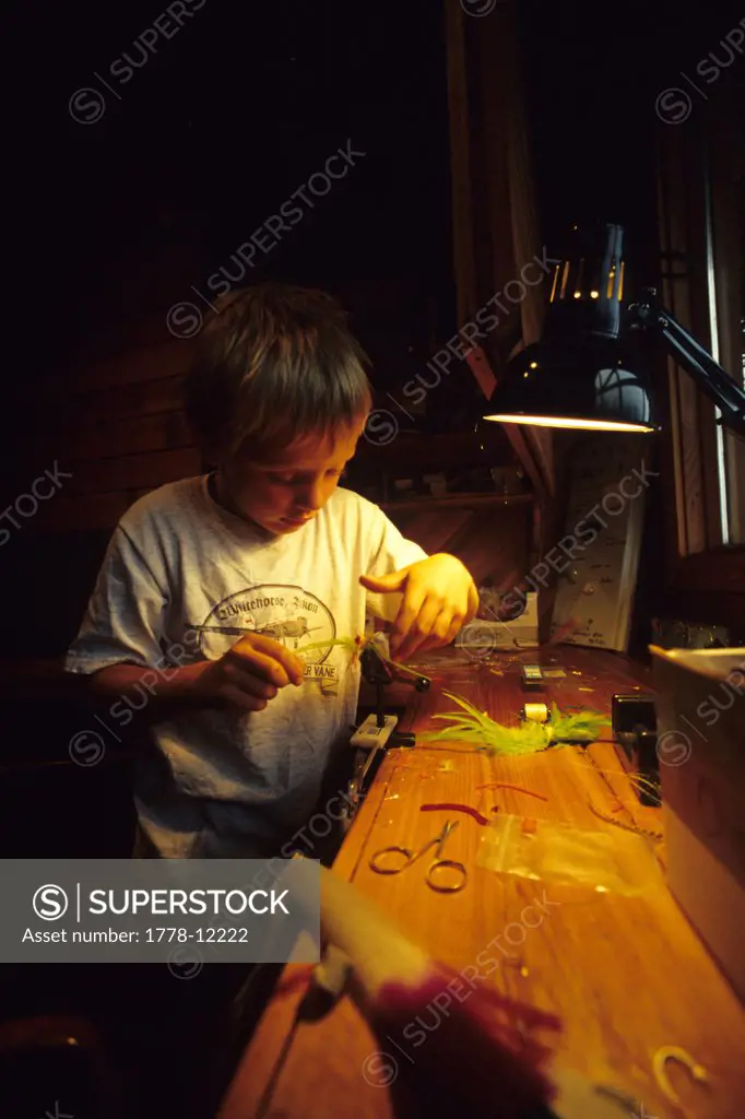 Young boy ties a fly-fishing fly at a fly-in fishing lodge in the Yukon Territory, Canada