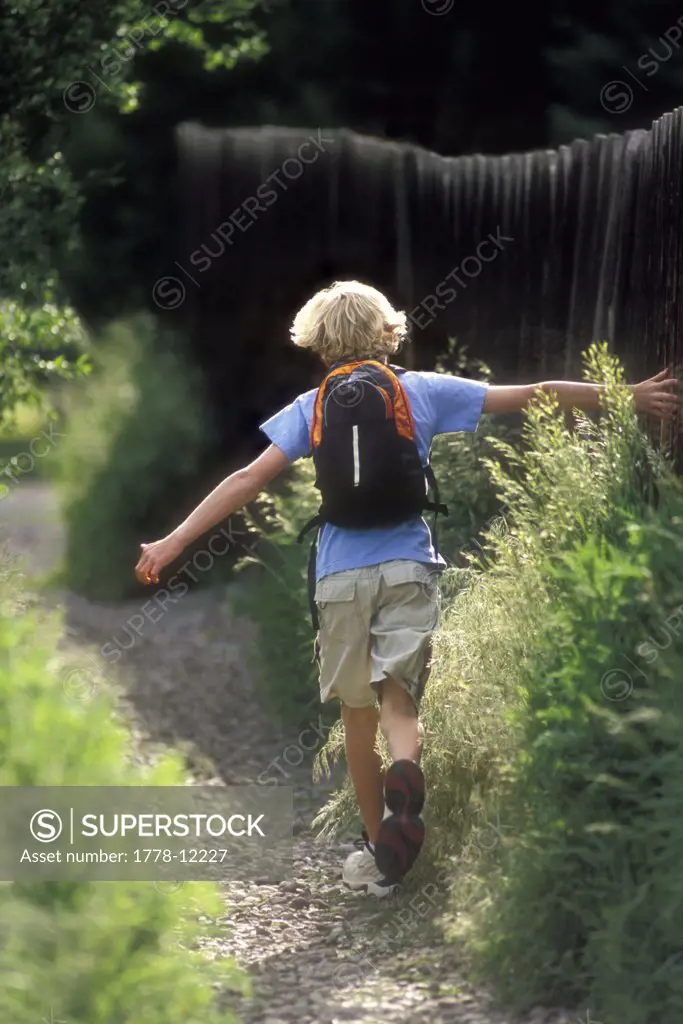 Young boy running on stone trail with his hands dragging along a wooden fence in El Jebel, Colorado