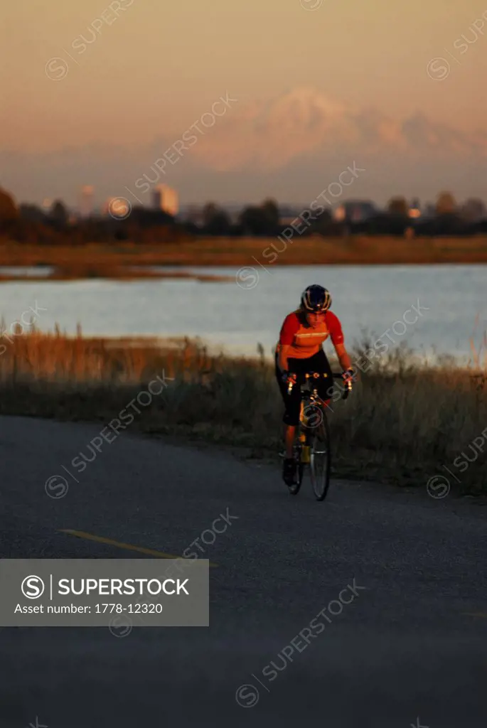 A woman is road cycling atsunset at Iona Beach, Richmond, British Columbia, Canada