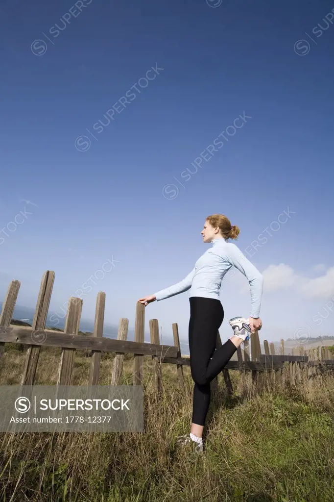 A young woman stretches before run along  the coastline of northern California near Mendocino, California