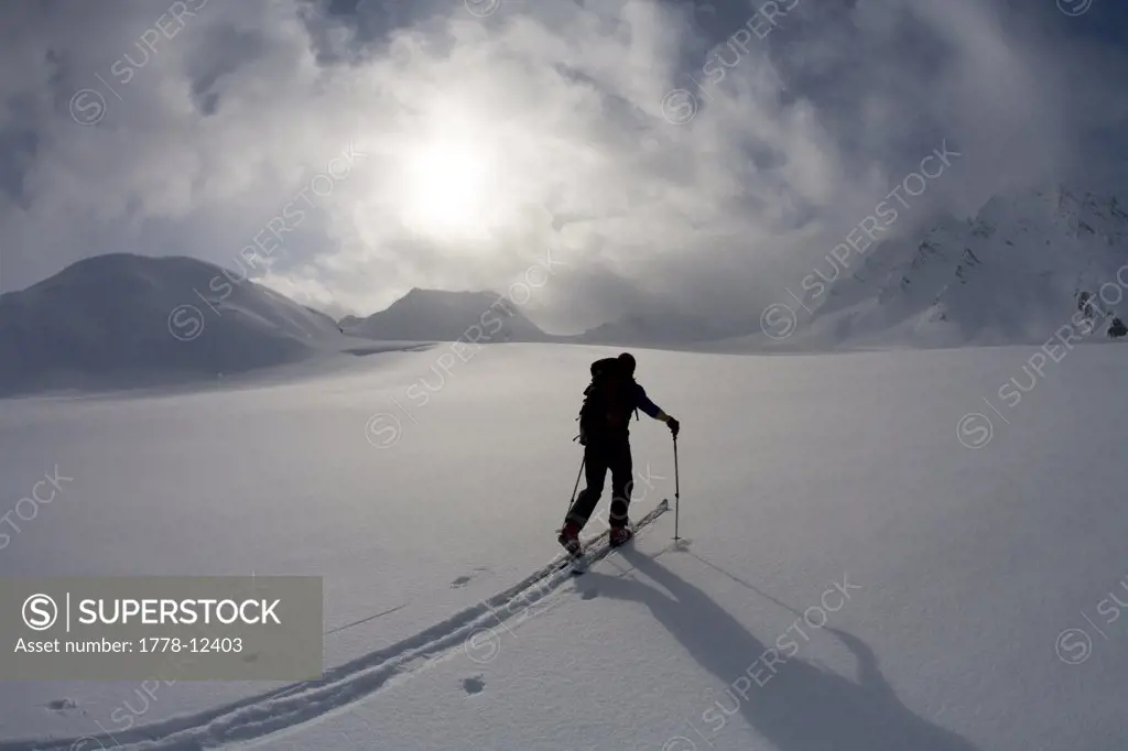Backcountry skier crosses glacier under late day stormy sky