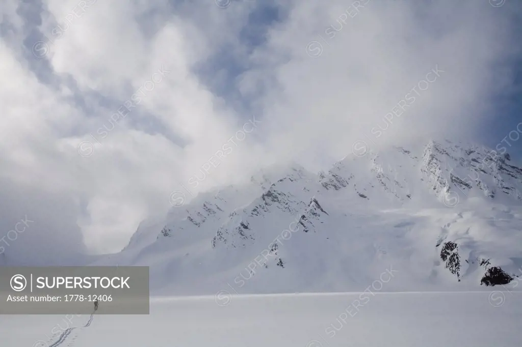 Backcountry skier crosses glacier under late day stormy sky