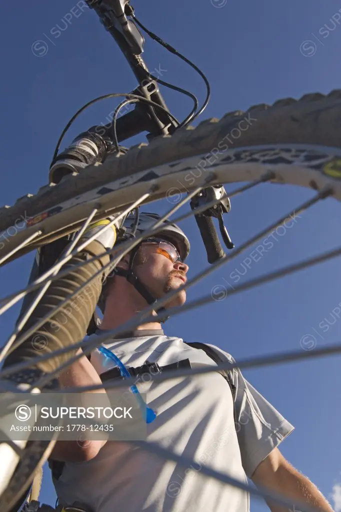 A portrait of a man through the mountain bike wheel that he is carrying