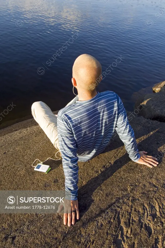 A man sitting at the edge of a lake listening to his iPod in the Finish Saimaa lake region