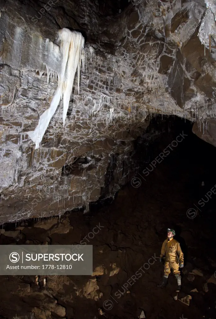 Cave explorer admires large cave formation called a Curtain high up on a wall in a cave in the Yorkshire Dales in England