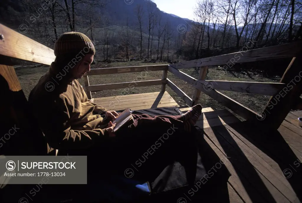 A male climber sitting on his crash pad and reading a book on a wooden porch near Jasper, Arkansas (Back Lit)